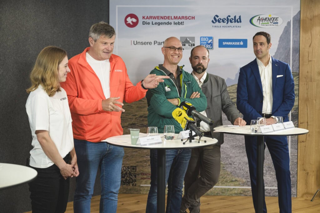 Personen bei einer Pressekonferenz mit Karwendelmarsch-Logo.